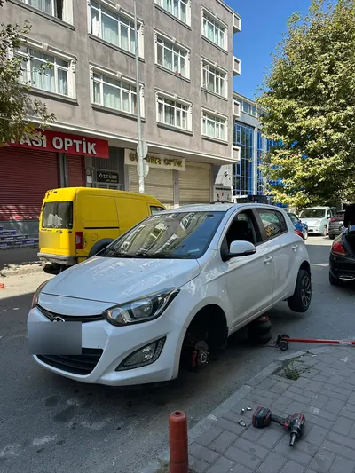 Gündüz cadde kenarında hatchback aracın ön tekeri sökülmüş hâlde lastik tamiri