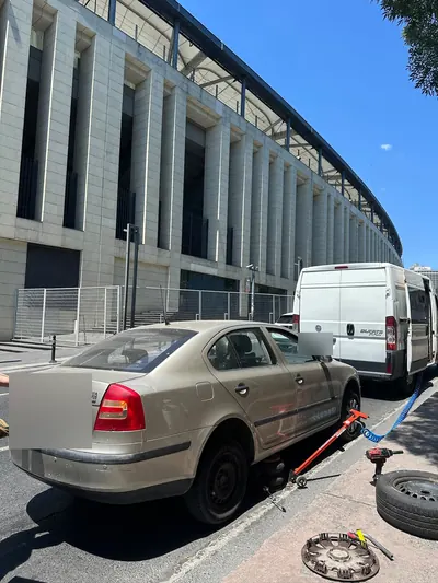 Stadyum yanında sedan aracın arka tekeri sökülmüş hâlde lastik değişimi