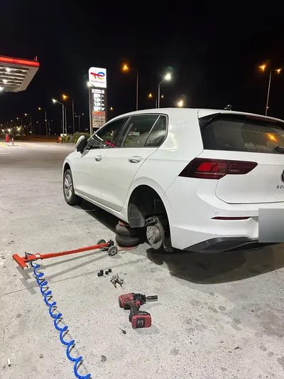 Gece akaryakıt istasyonunda hatchback aracın arka tekeri sökülmüş hâlde lastik tamiri